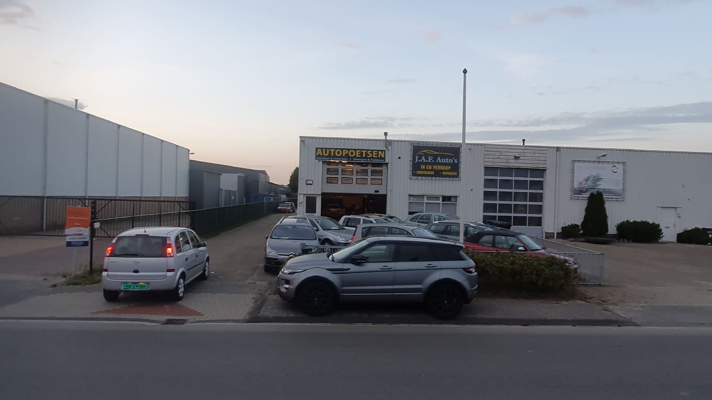 De gevel van J.A.F. Auto's in de avond, met verlichte werkplaats en auto's op het terrein
